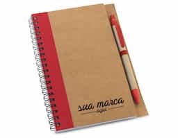 Caderno B6 espiral de capa dura em cartão, com 120 páginas lisas em papel reciclado e suporte para esferográfica (inclusa). 