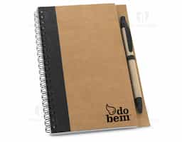 Caderno B6 espiral de capa dura em cartão, com 120 páginas lisas em papel reciclado e suporte para esferográfica (inclusa). 