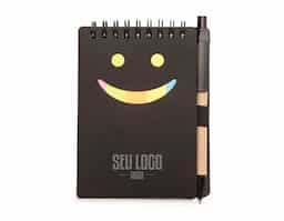 Bloco de anotações ecológico com caneta de papelão. Possui detalhe "smile" na capa frontal(verso liso), caneta ecológica com acabamentos em plástico acionada por clique, primeira folha(branca) com cinco blocos autoadesivos coloridos com aproximadamente 20 folhas cada, bloco amarelo com aproximadamente 20 folhas e 70 folhas brancas pautadas.