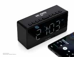 Caixa de som multimídia com relógio despertador e suporte para celular. Produzida em plástico e com borrachas antiderrapantes na área inferior, a caixa de som tem a área frontal com display de LED, além de um compartimento com suporte para celular – uma espécie de "gaveta" aonde é exibido (MUSIC), basta puxá-la ter acesso ao compartimento. A caixa de som executa nos modos bluetooth, rádio FM, cartão TF-microSD e entrada auxiliar P2. Acompanha cabo USB e manual em inglês.