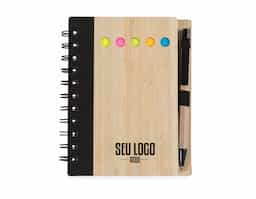 Bloco de anotações ecológico com caneta e autoadesivos. Capa de bambu com uma faixa preta no lado esquerdo e verso liso. Possui cinco blocos autoadesivos coloridos com aproximadamente 20 folhas cada, 70 folhas aproximadamente brancas pautadas com logo reciclado na lateral inferior. Acompanha suporte elástico de nylon com uma caneta de papelão com acessórios plásticos.