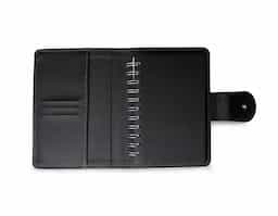 Caderneta de couro sintético com fechamento de botão. Possui caderno capa dura em couro sintético com aproximadamente 100 folhas pautadas, divisórias para cartões e bolso lateral.