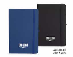 Planner com capa dura emborrachada, marca-páginas em fita de cetim, elástico para fechamento e suporte para caneta. Apresenta páginas dedicadas a dados pessoais, calendários de 2025 até 2027 e espaço para anotações diárias e semanais ao longo de todo ano de 2026.