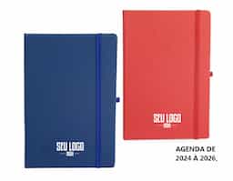 Planner com capa dura em cromato, marca-páginas em fita de cetim, elástico para fechamento e suporte para caneta. Apresenta páginas dedicadas a dados pessoais, calendários de 2025 a 2027 e espaço para anotações diárias e semanais ao longo de todo o ano de 2026.