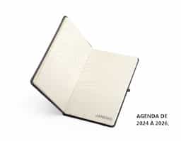 Planner com capa dura em cromato, marca-páginas em fita de cetim, elástico para fechamento e suporte para caneta. Apresenta páginas dedicadas a dados pessoais, calendários de 2025 a 2027 e espaço para anotações diárias e semanais ao longo de todo o ano de 2026.