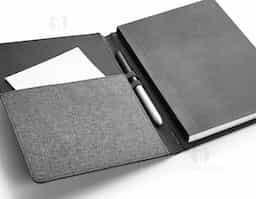 Pasta em tecido poliéster com caderno. Caderno removível com 80 folhas não pautadas. Com bolso interior e porta esferográfica. Fornecida em embalagem de non-woven. Esferográfica não inclusa