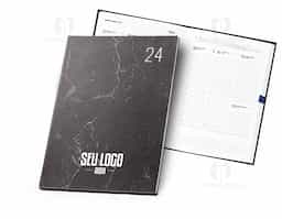 Agenda B5 com capa rígida em papel pedra e marcador em fita, com aspeto mármore e cantos retos. Está organizada num plano semanal. 175 x 245 mm
