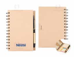 Um caderno de capa dura em papelão com porta-canetas elástico, encadernação Wire-O e dois bolsos interiores. Contém aproximadamente 70 folhas brancas com pauta além de um bloco com cerca de 20 folhas amarelas autoadesivas. Inclui também seis blocos de marcadores de página coloridos autoadesivos com cerca de 20 unidades cada. Acompanha uma caneta esferográfica com carga azul de 1.0mm com acionamento por clique, corpo em papelão e demais componentes feitos em plástico.