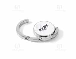 Suporte de bolsa em metal resistente, ideal para manter sua bolsa sempre por perto e longe do chão. Pode ser apoiado em superfícies como mesas para pendurar a alça com segurança. Quando não está em uso, recolhe-se de forma compacta e se mantém fixo à base por um ímã discreto e funcional.
