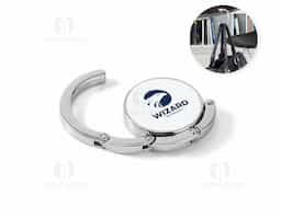 Suporte de bolsa em metal resistente, ideal para manter sua bolsa sempre por perto e longe do chão. Pode ser apoiado em superfícies como mesas para pendurar a alça com segurança. Quando não está em uso, recolhe-se de forma compacta e se mantém fixo à base por um ímã discreto e funcional.