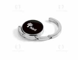 Suporte de bolsa em metal resistente, ideal para manter sua bolsa sempre por perto e longe do chão. Pode ser apoiado em superfícies como mesas para pendurar a alça com segurança. Quando não está em uso, recolhe-se de forma compacta e se mantém fixo à base por um ímã discreto e funcional.