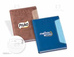 Agenda diária 2026 com capa em couro sintético e marca-páginas em fita de cetim. Contém páginas dedicadas para dados pessoais, calendários de 2025 a 2027, lista de contatos, planejamento e mapas.